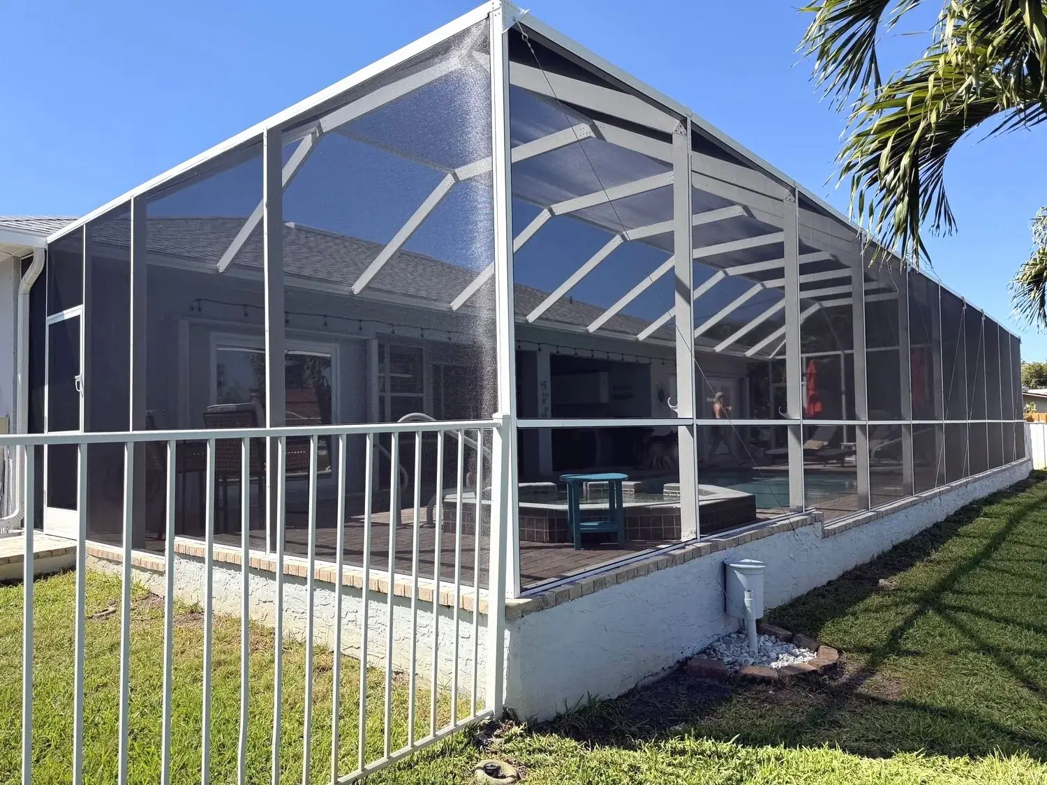 Freshly painted white pool cage seen from the lawn, new screen panels, pool and patio furniture inside, palms behind