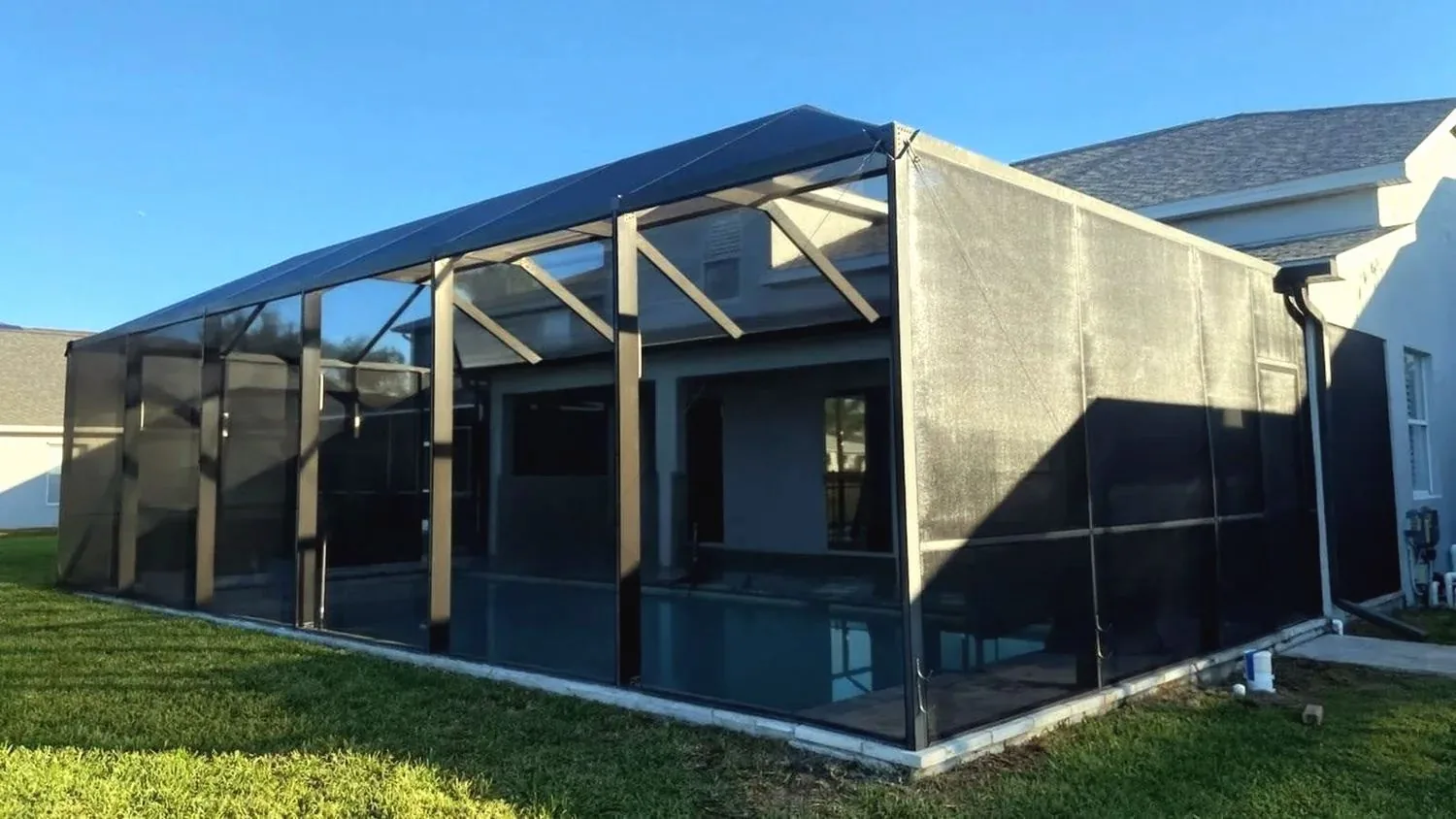 New black pool cage on a gray house at sunset, seen from the lawn, bronze corner posts and dark mesh