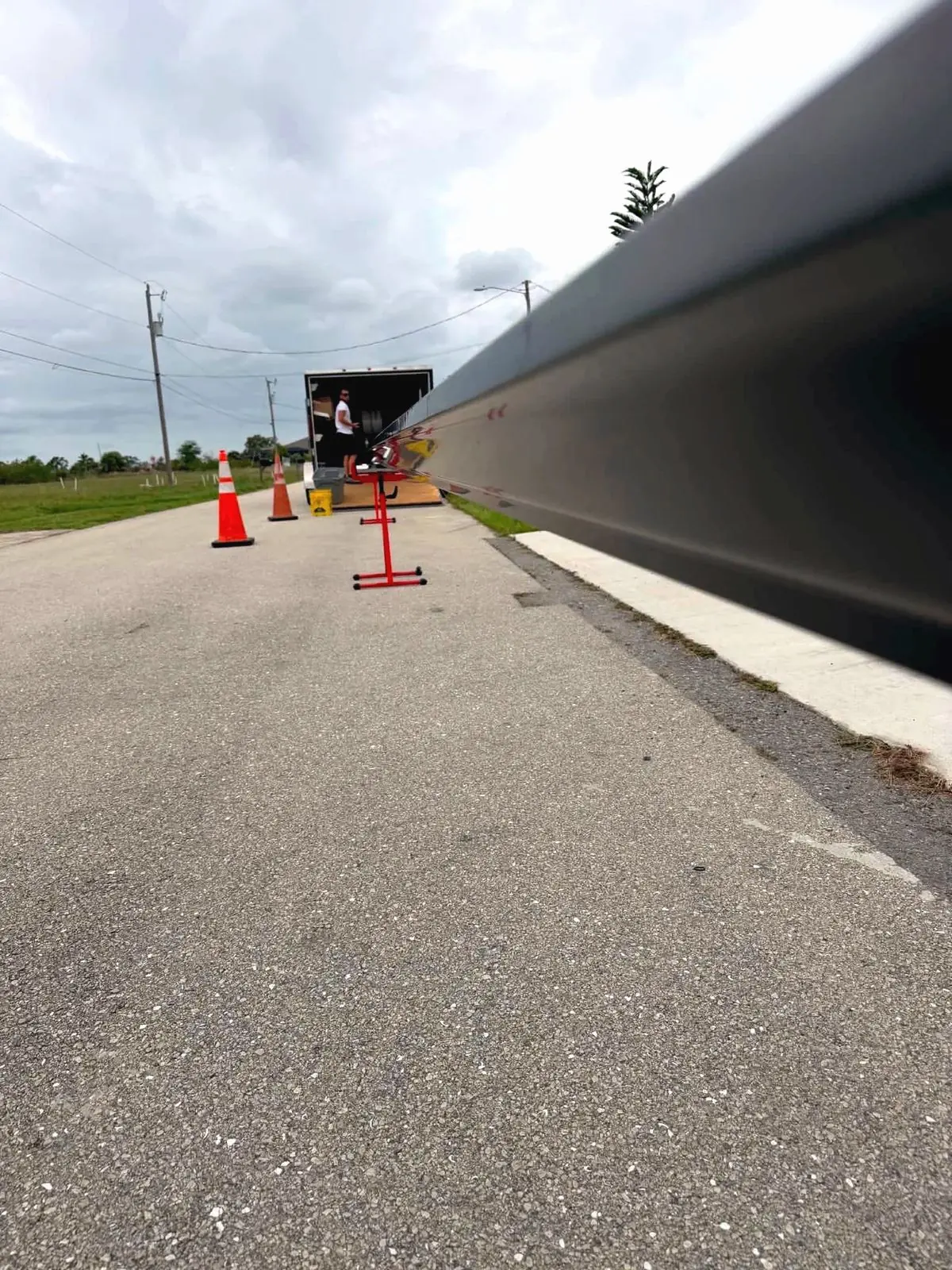 Looking down a freshly rolled dark gutter run toward the gutter machine trailer, cones and a stand on the road, overcast sky