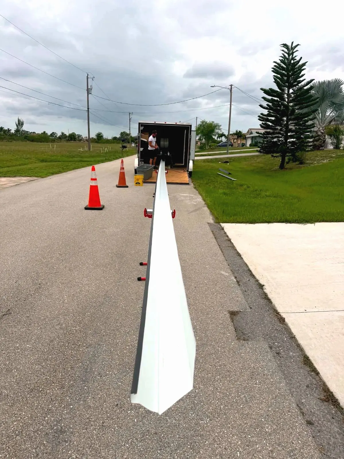 Long white seamless gutter run coming off the gutter machine inside an enclosed trailer, orange cones on the street, cloudy sky