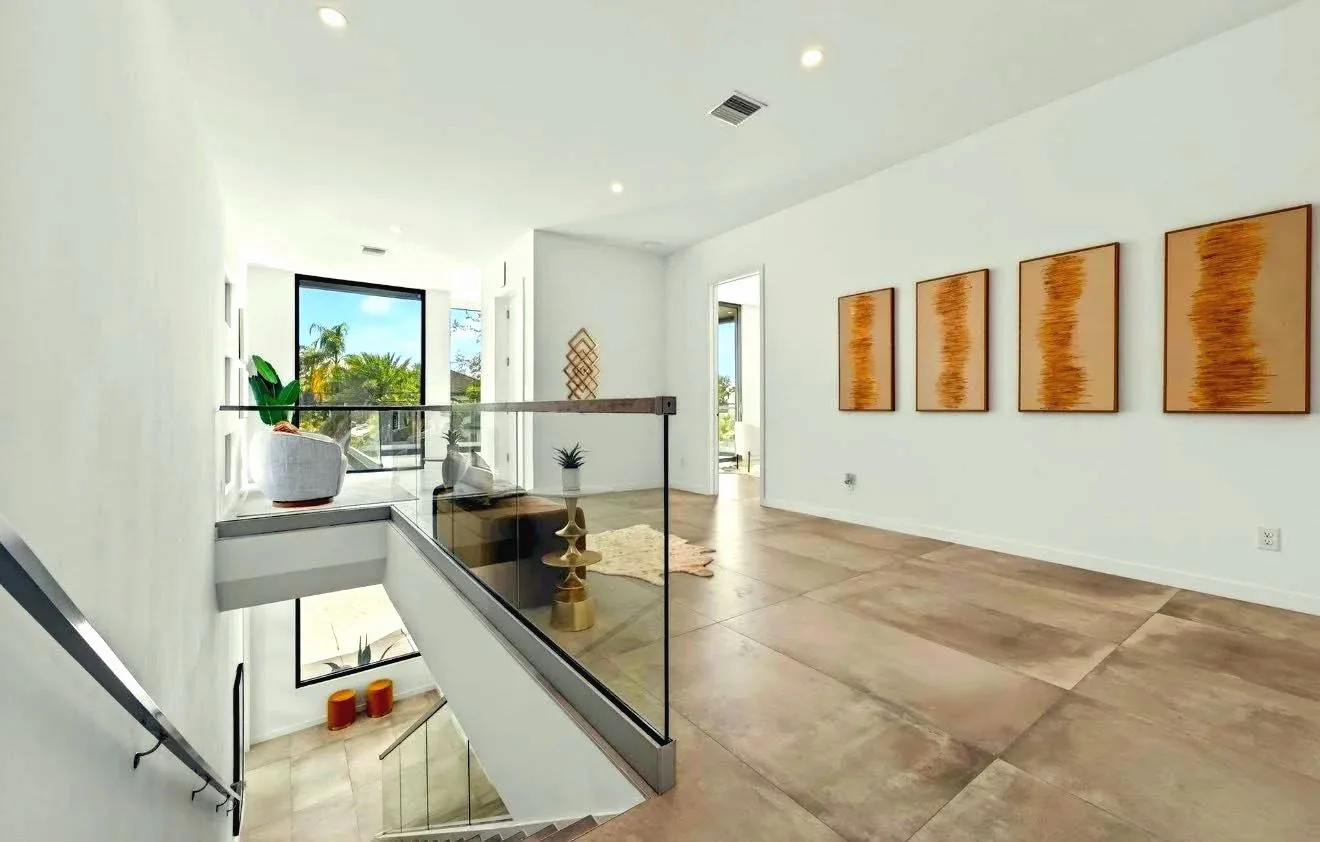 Frameless glass railing around a stair opening in a modern interior with wood-look tile floors and four framed prints on the wall