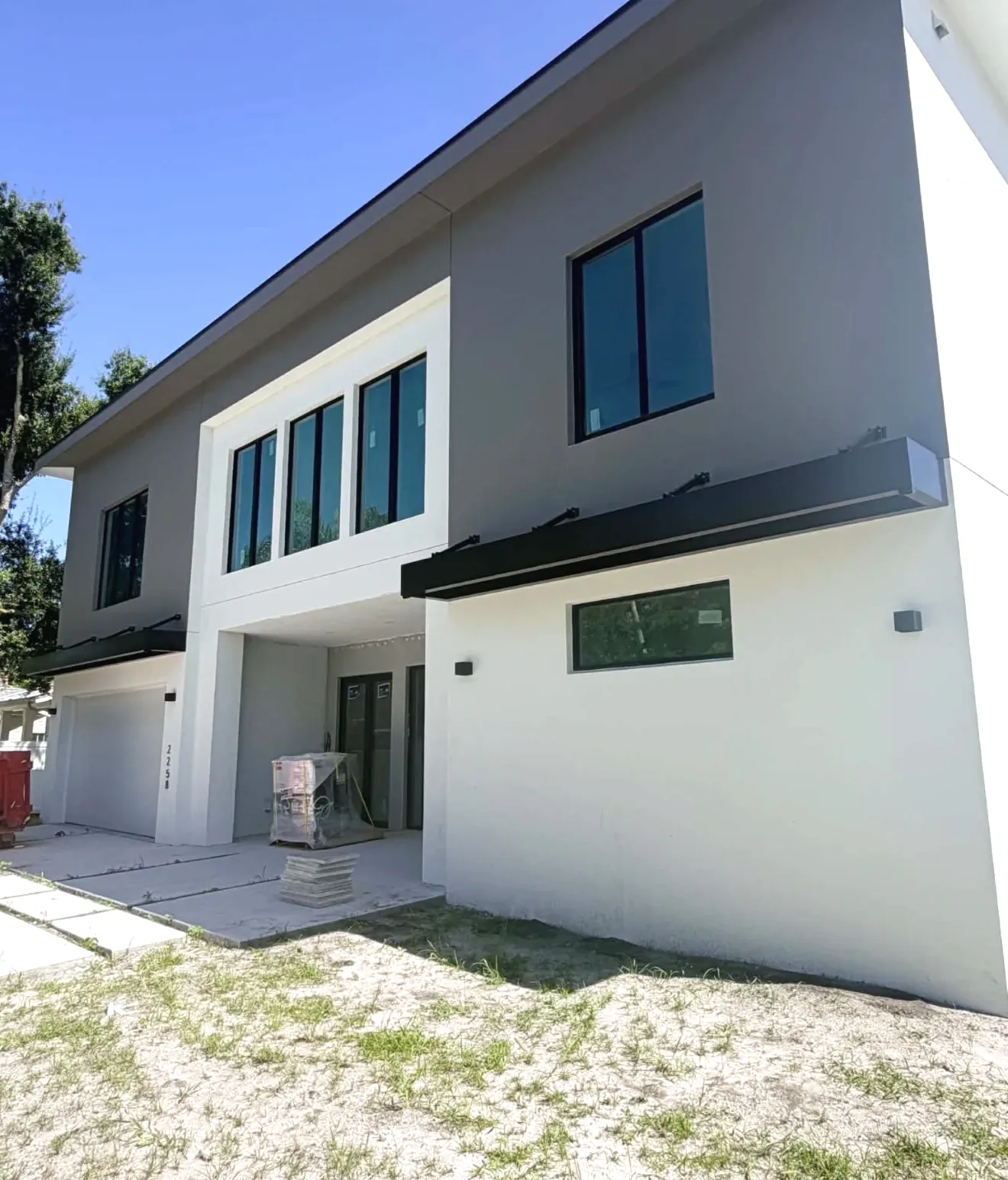 Dark aluminum overhang panels on brackets above windows of a two-story gray and white stucco home under construction