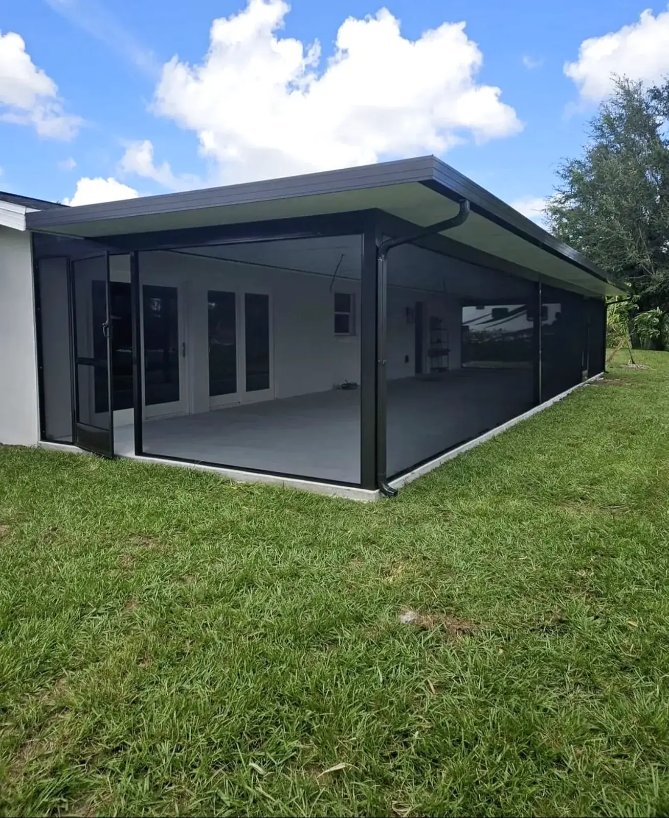 Bronze aluminum screen room with a flat insulated roof and gutter attached to a white house, green lawn around it