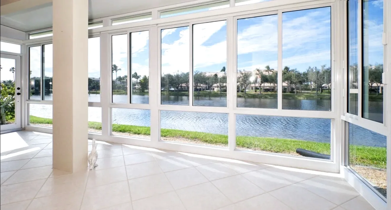 Interior of an enclosed lanai with white framed sliding windows, tile floor and a lake view across the glass