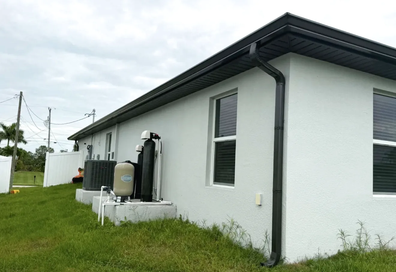 Dark bronze seamless gutter and downspout running down the corner of a white stucco single story house.