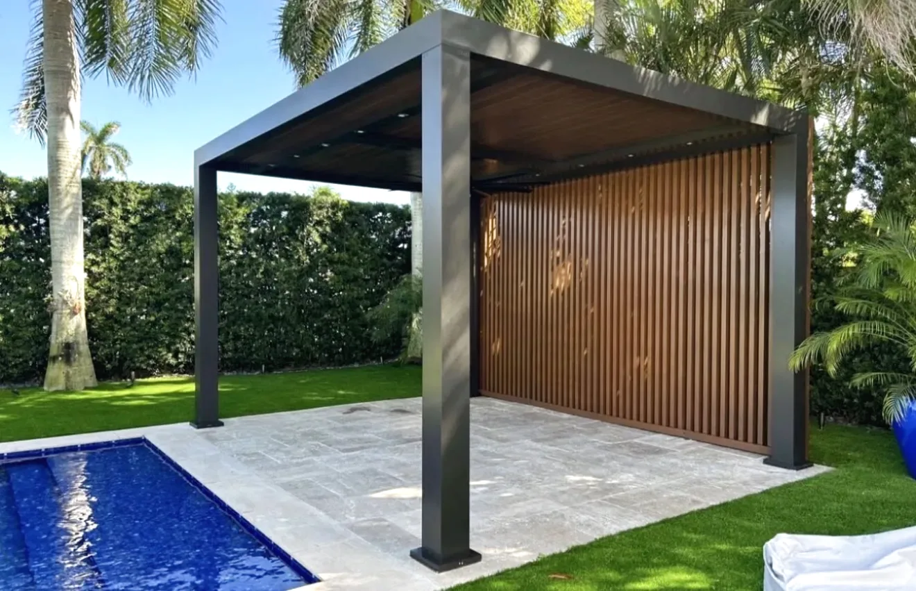 Dark grey aluminum louvered pergola with wood look slat privacy screen on a paver patio beside a pool