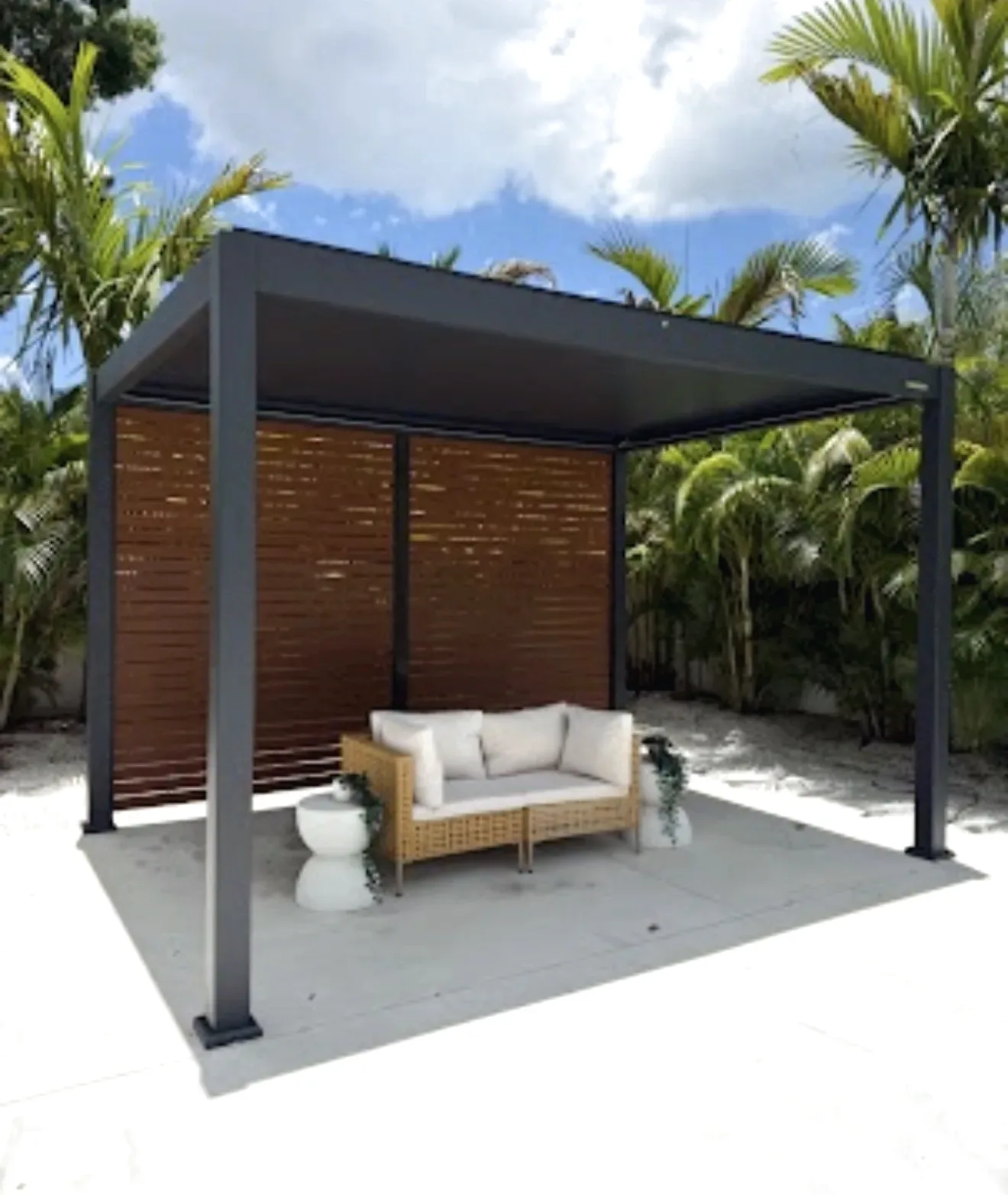 Freestanding grey aluminum louvered pergola with wood look privacy screens sheltering a wicker sofa on a concrete pad