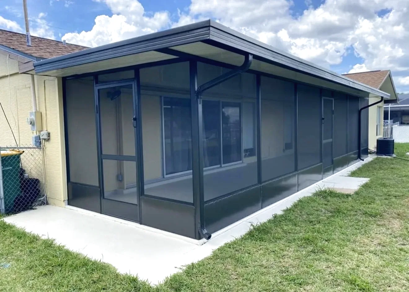 Bronze aluminum screen room with solid roof panels and gutter attached to a single story yellow stucco house