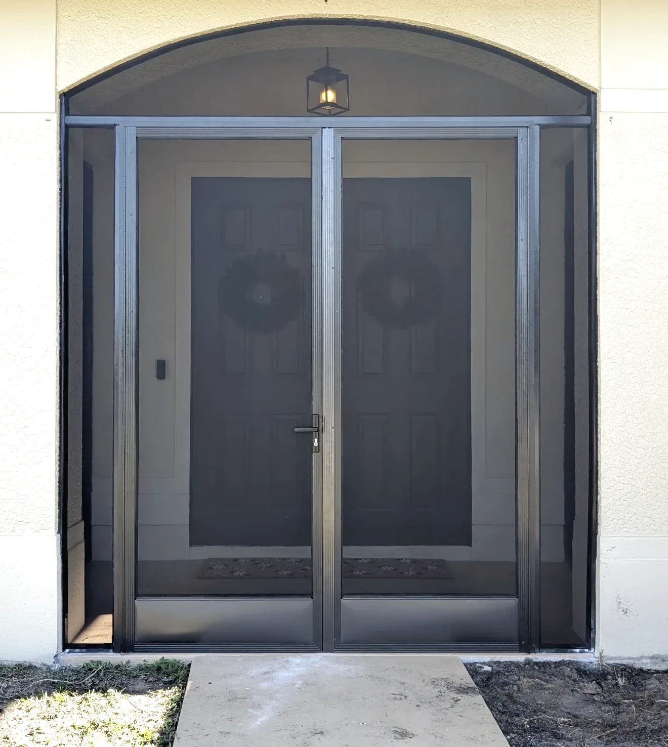 Bronze aluminum screen enclosure framing an arched front entry, with hinged screen door and fixed side panels