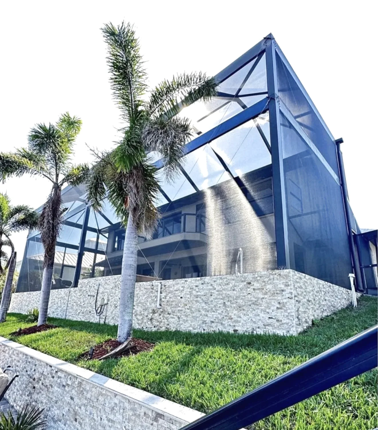 Two story bronze screen enclosure attached to a home, stacked stone knee wall, royal palms and lawn in Southwest Florida.
