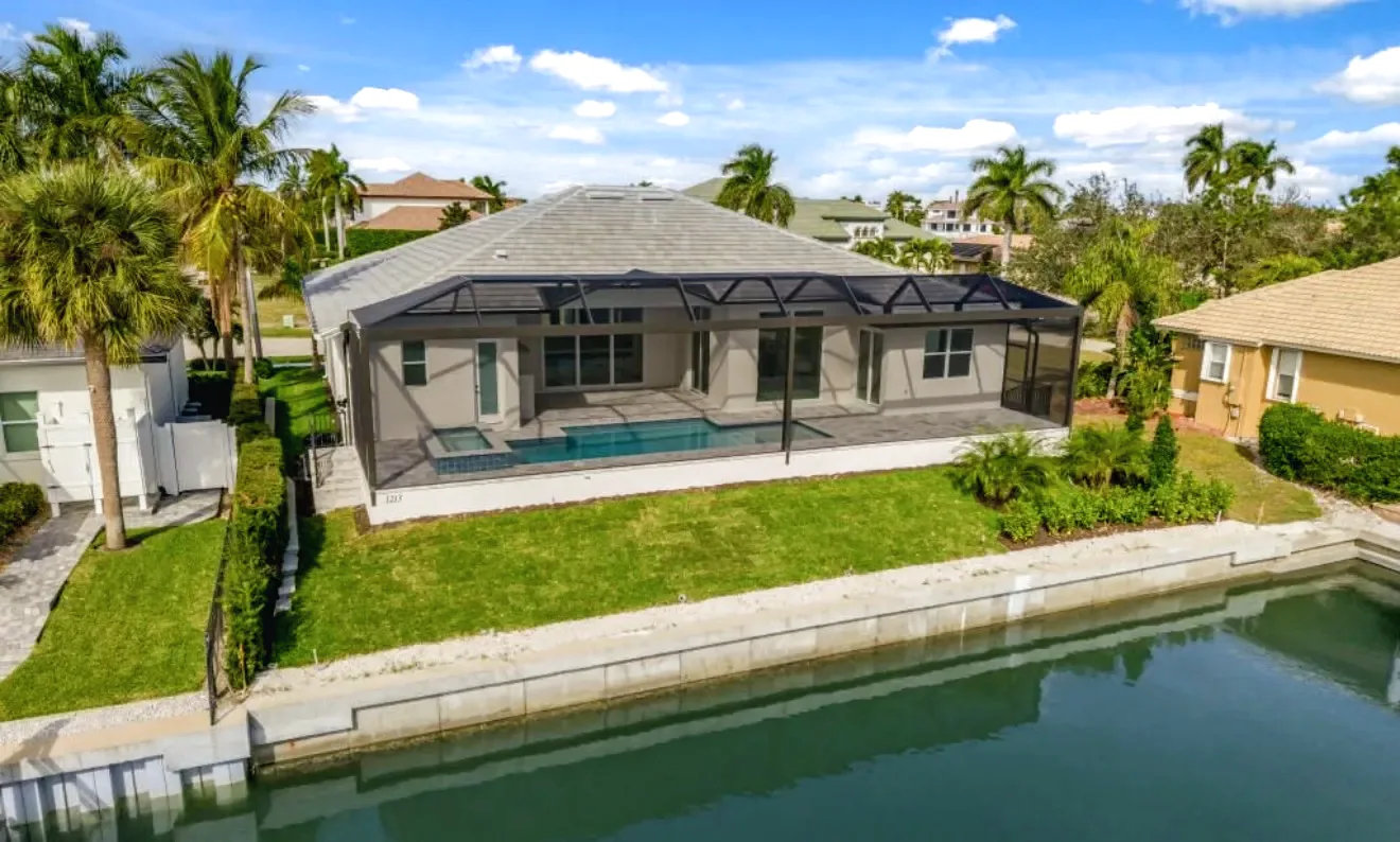 Aerial view of a canal front home with a dark screen enclosure over the pool, lawn and seawall in Southwest Florida.