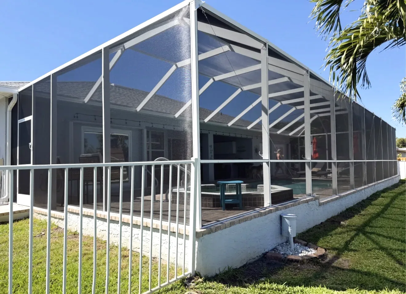 Exterior side view of a white aluminum gable screen enclosure over a pool and spa, white aluminum fence and lawn