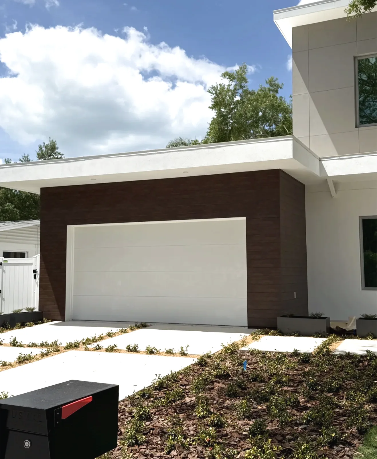 Dark wood-grain siding panels wrapping a garage bay on a white stucco home with a white sectional garage door