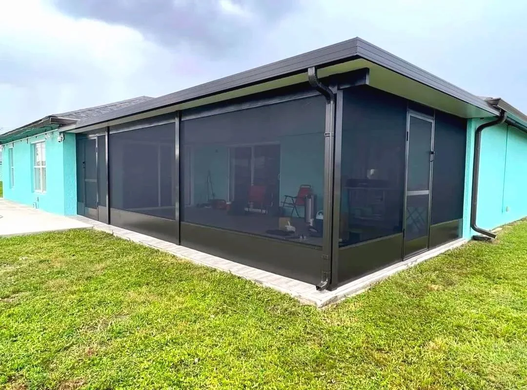 Bronze aluminum lanai with a solid roof on the back of a teal house, screen door at the corner, gray sky
