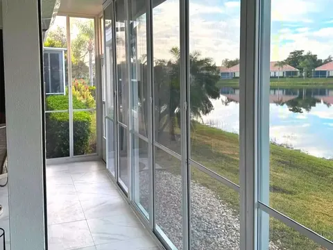 White aluminum framed acrylic sliding panels enclose a tiled lanai with river rock beds and a lake beyond