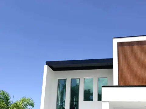 Deep black flat overhang wrapping the upper story of a white stucco home with tall windows and palms nearby