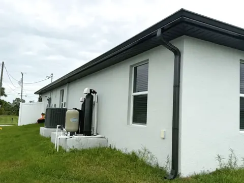 Dark bronze seamless gutter and downspout running down the corner of a white stucco single story house.