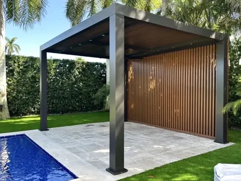 Dark grey aluminum louvered pergola with wood look slat privacy screen on a paver patio beside a pool