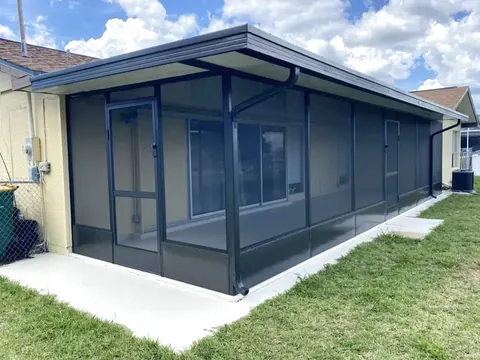 Bronze aluminum screen room with solid roof panels and gutter attached to a single story yellow stucco house