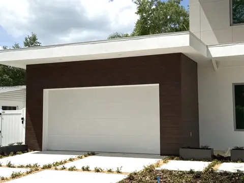 Dark wood-grain siding panels wrapping a garage bay on a white stucco home with a white sectional garage door